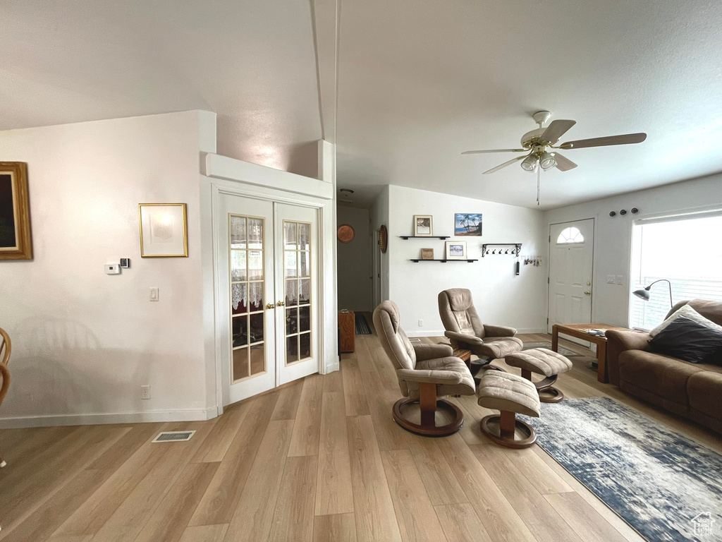 Living room featuring french doors, ceiling fan, baseboards, light wood-type flooring, and lofted ceiling