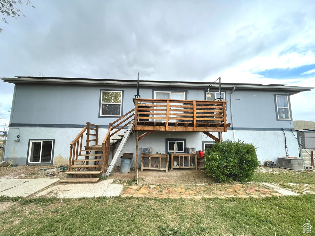 Back of property with a wooden deck, stucco siding, stairway, a lawn, and central AC