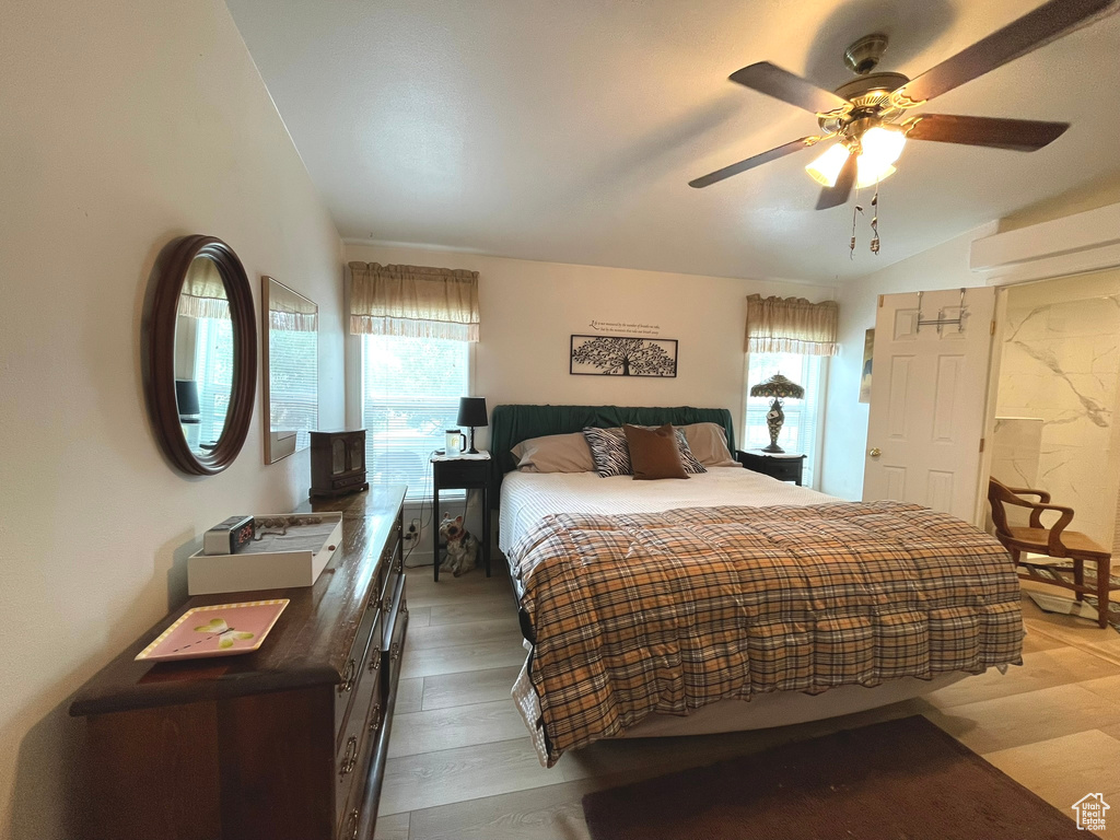 Bedroom with ceiling fan, light wood-style floors, a wood stove, and lofted ceiling