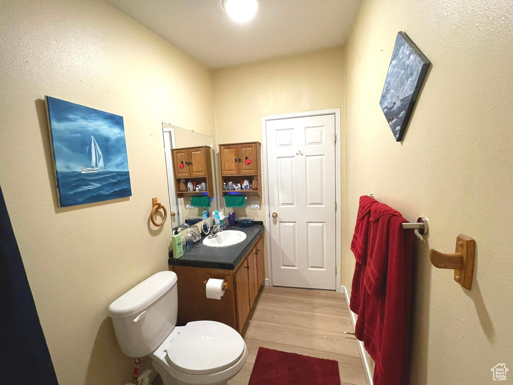 Half bathroom with toilet, vanity, and wood finished floors