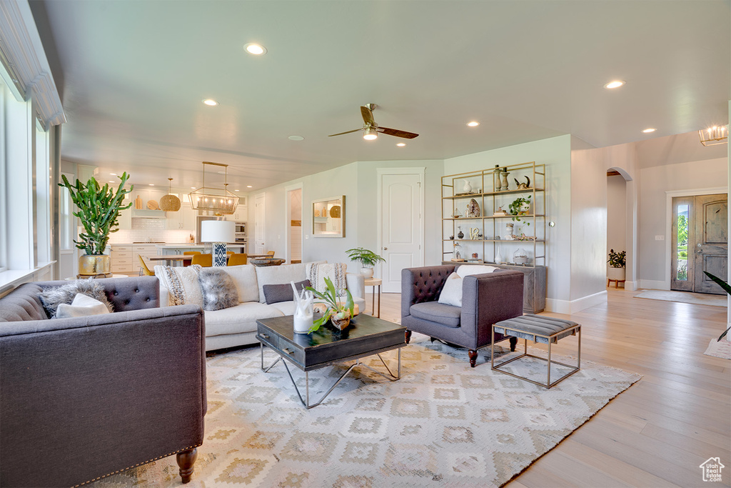Living area featuring arched walkways, light wood finished floors, recessed lighting, ceiling fan, and a chandelier