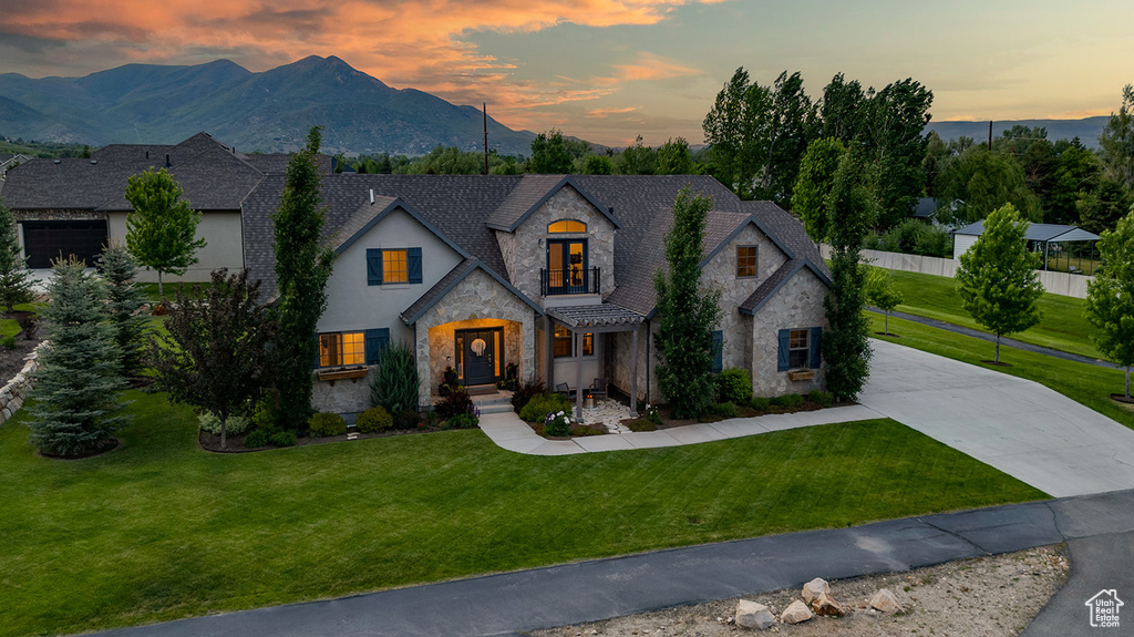 French country home with stone siding, a front yard, stucco siding, driveway, and a mountain view