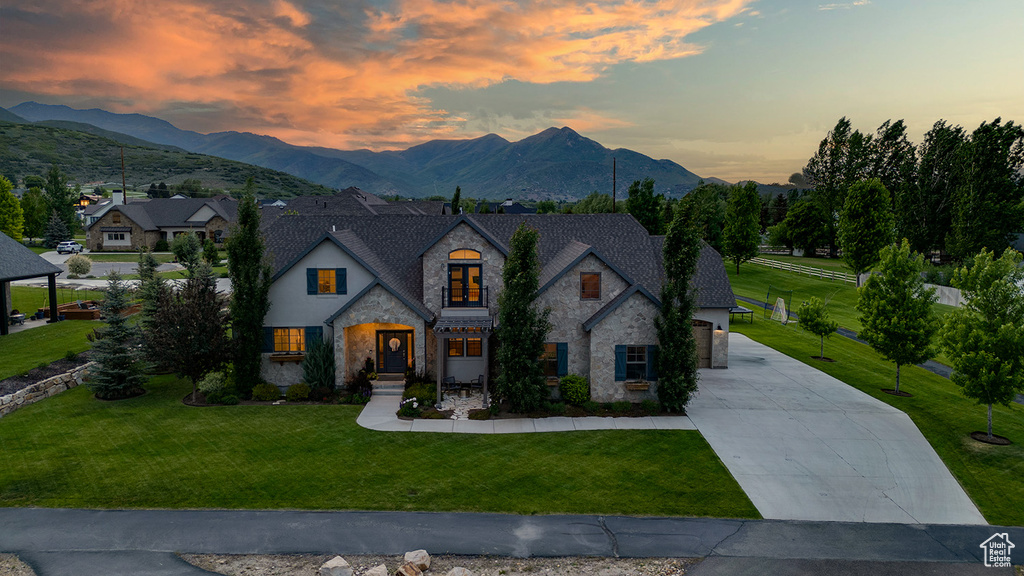 French country inspired facade featuring stone siding, driveway, a mountain view, and a front lawn