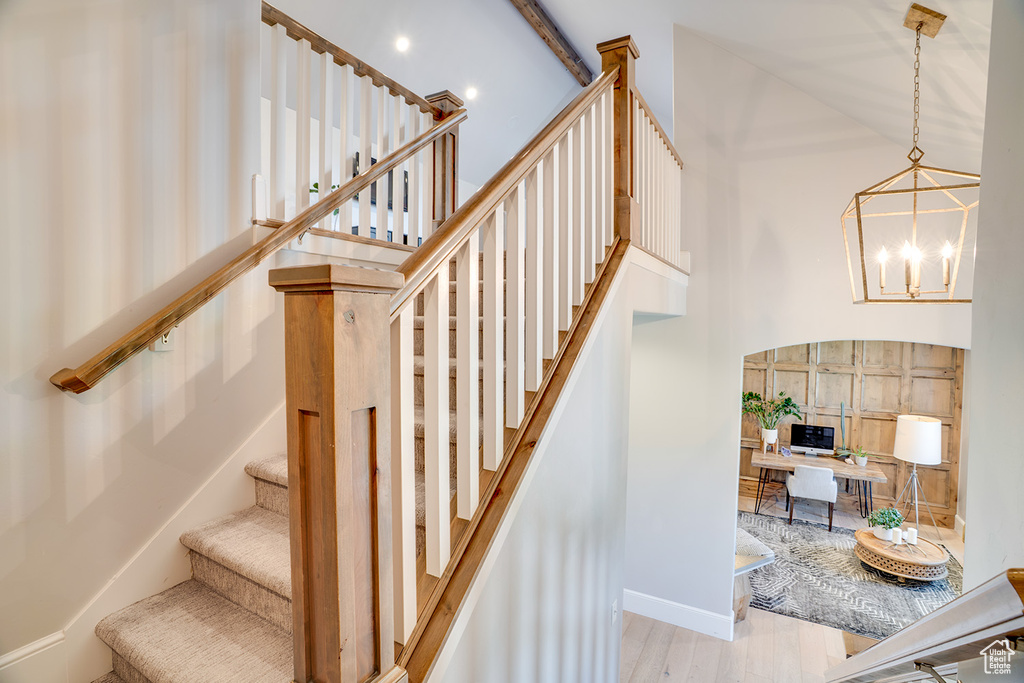 Stairs featuring wood finished floors, a chandelier, and a towering ceiling