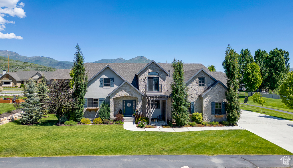 French country home featuring stone siding, a front yard, driveway, and a mountain view