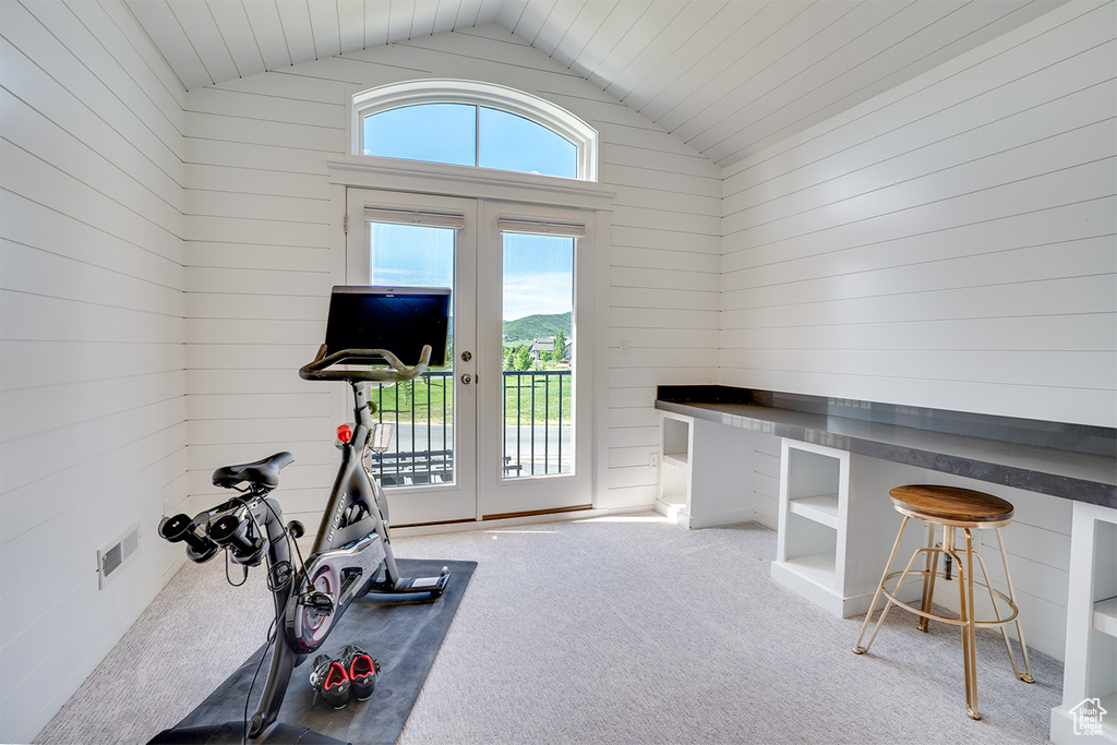 Exercise room featuring french doors, lofted ceiling, carpet floors, and wooden walls