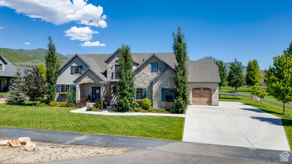 View of front of property featuring stone siding, driveway, an attached garage, a front yard, and stucco siding