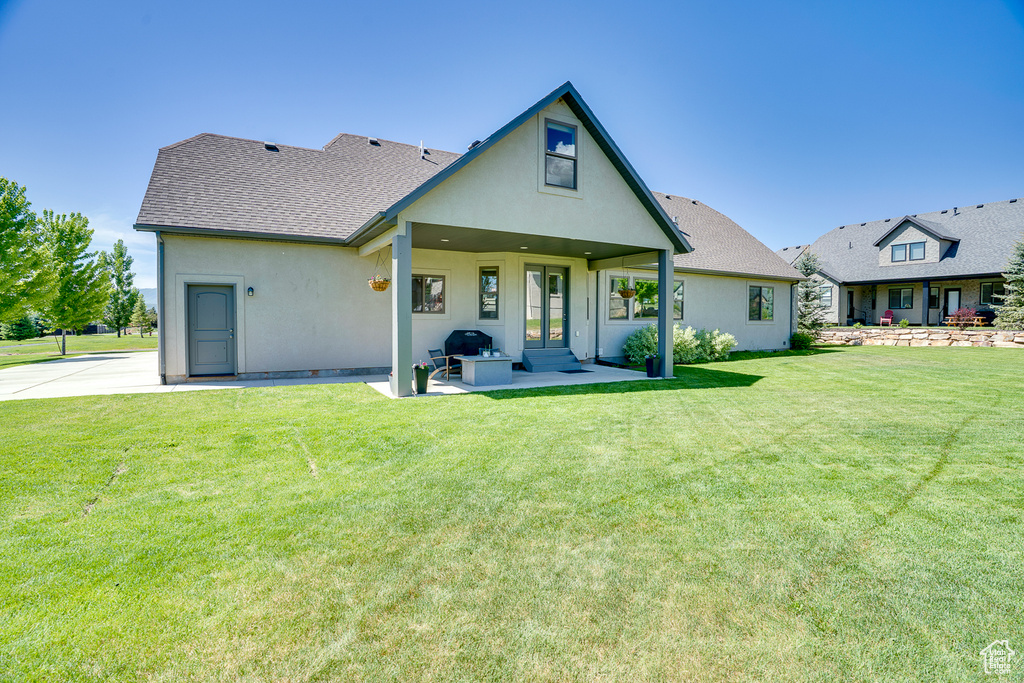 Rear view of house featuring stucco siding, a yard, roof with shingles, and a patio area