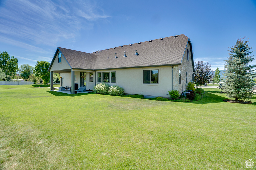 Rear view of property featuring a lawn, roof with shingles, a patio area, and stucco siding