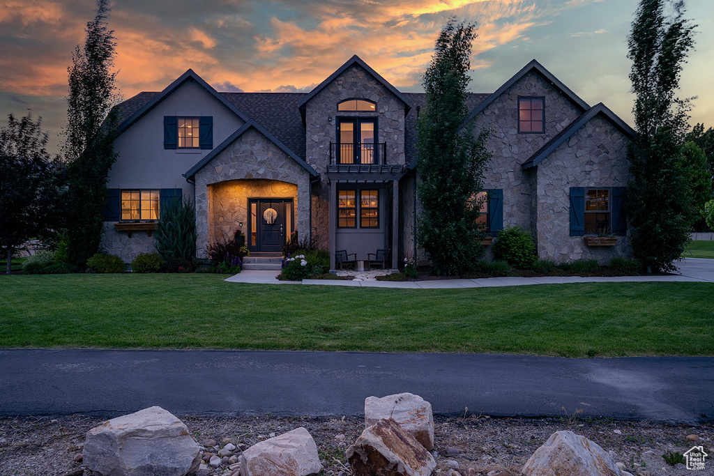 French country style house with stone siding, a balcony, a front lawn, and stucco siding