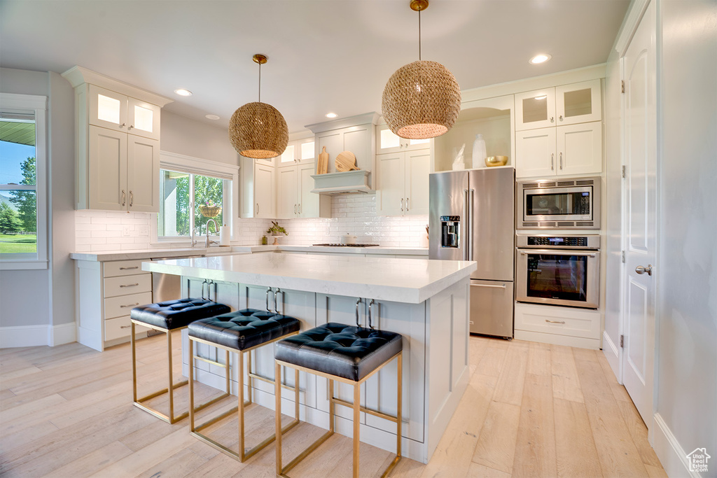 Kitchen with appliances with stainless steel finishes, light countertops, decorative backsplash, baseboards, and light wood-style floors