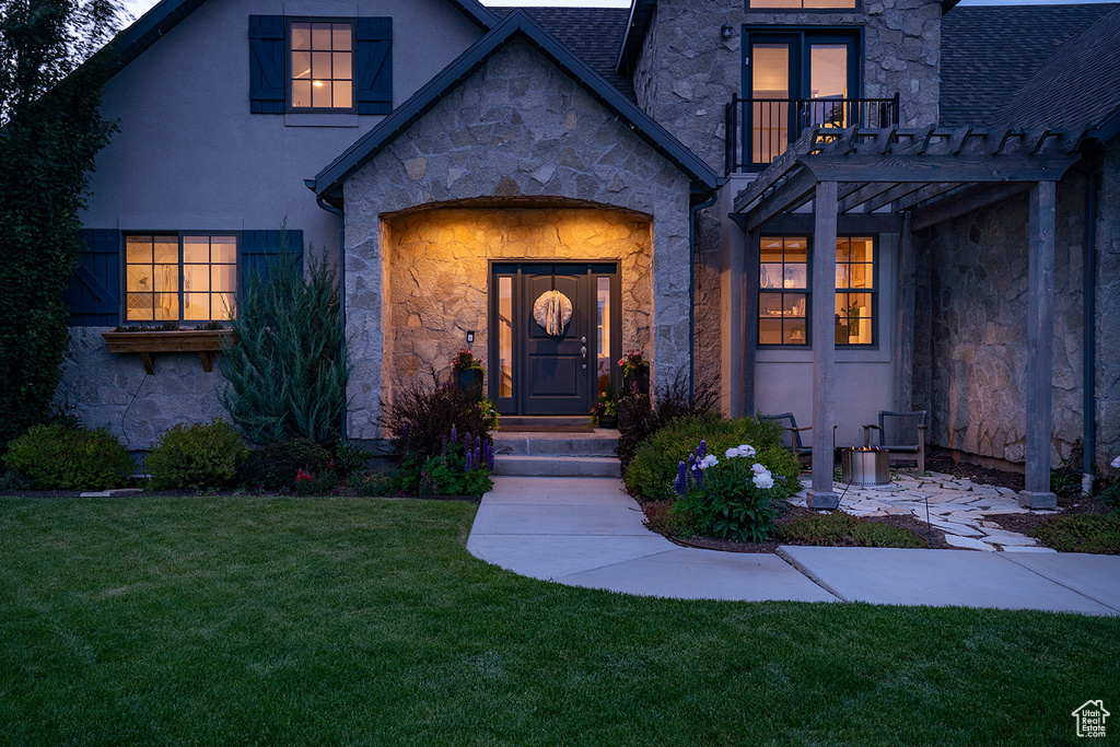 Doorway to property featuring stone siding, a yard, stucco siding, and a balcony