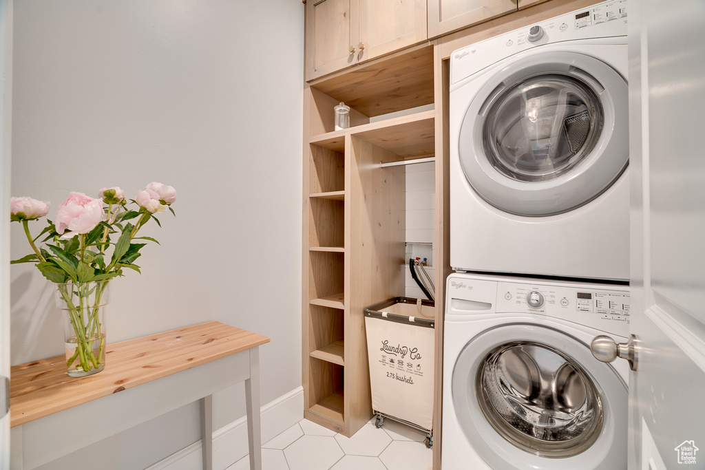 Laundry room featuring stacked washer and clothes dryer, cabinet space, and light tile patterned floors