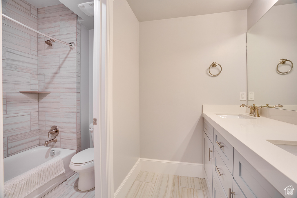Bathroom featuring toilet, double vanity,  shower combination, and baseboards