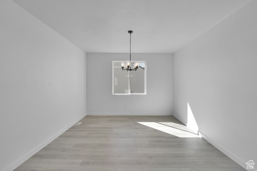 Unfurnished dining area featuring a chandelier, light wood-style flooring, and baseboards
