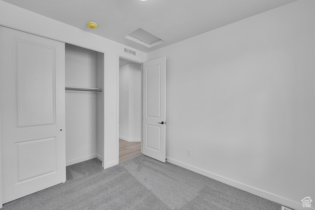 Unfurnished bedroom featuring carpet floors, attic access, baseboards, and a closet
