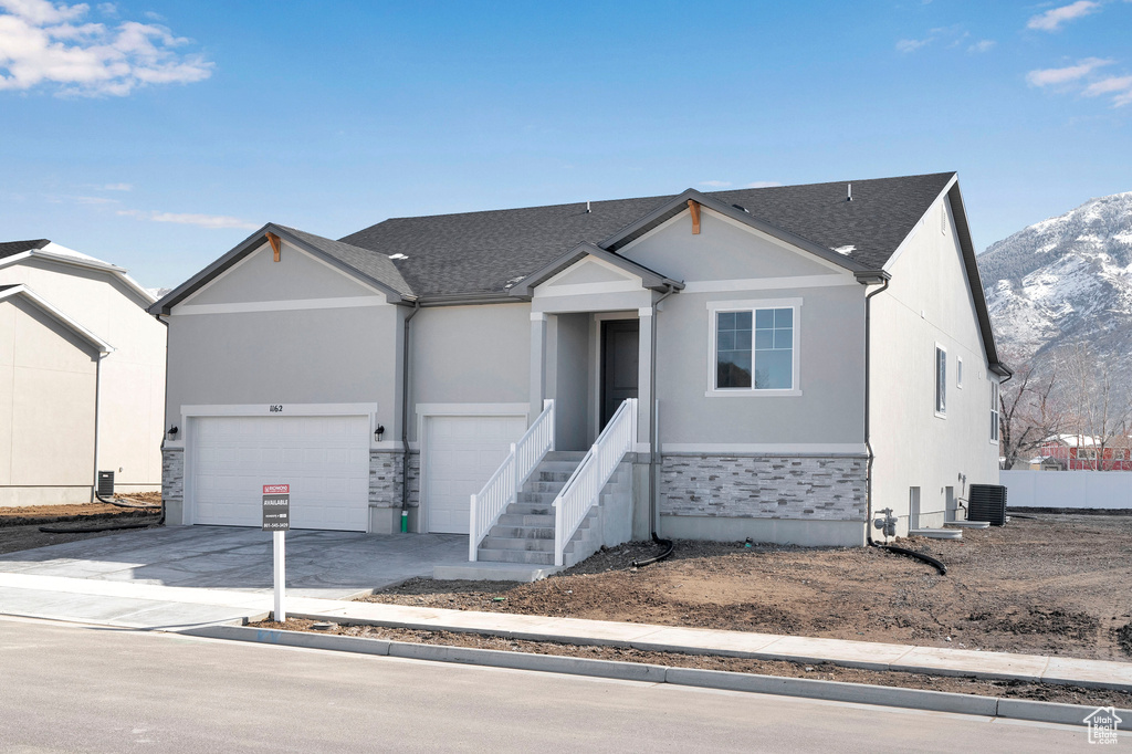 Ranch-style home featuring stone siding, a mountain view, concrete driveway, an attached garage, and central AC unit