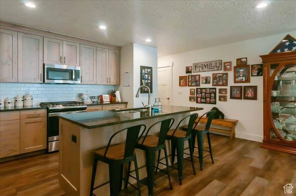 Kitchen with appliances with stainless steel finishes, a sink, dark countertops, dark wood-style flooring, and decorative backsplash
