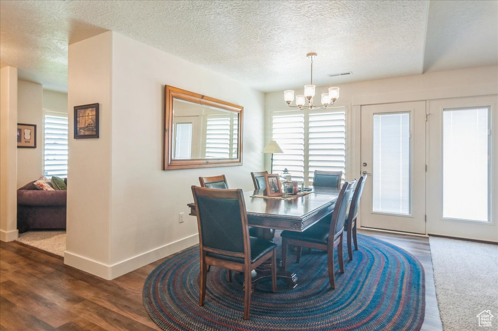 Dining room with a chandelier, a textured ceiling, baseboards, and dark wood-style flooring