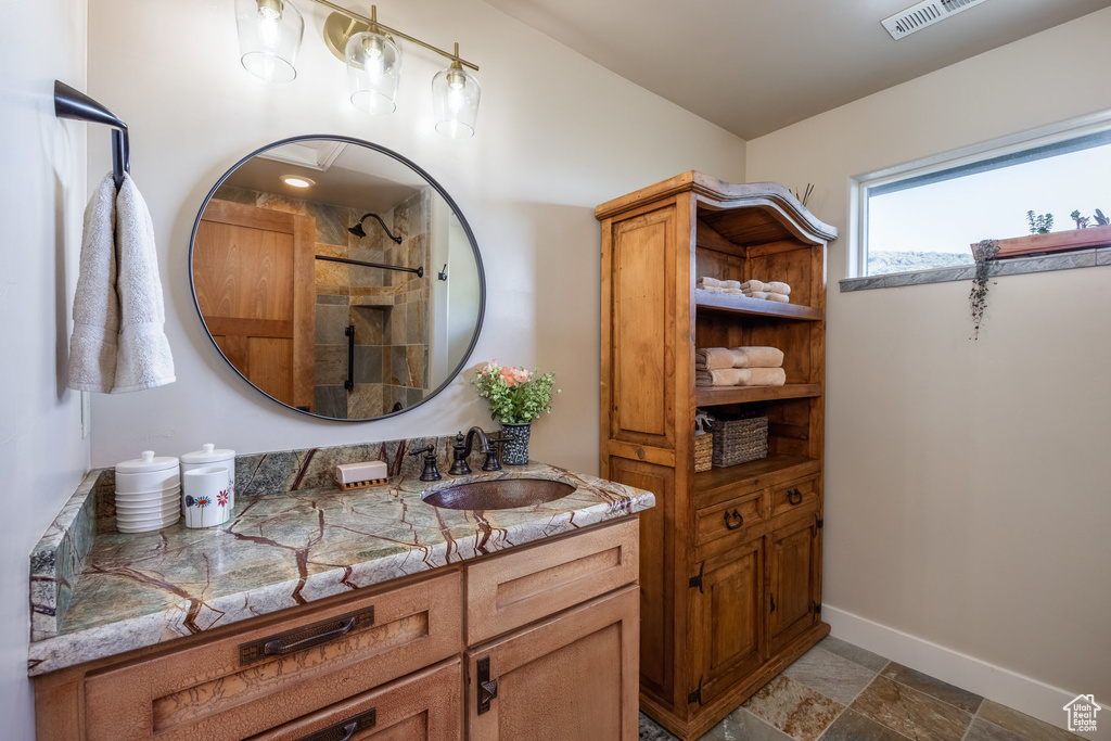 Full bathroom featuring vanity, a tile shower, baseboards, and stone finish flooring
