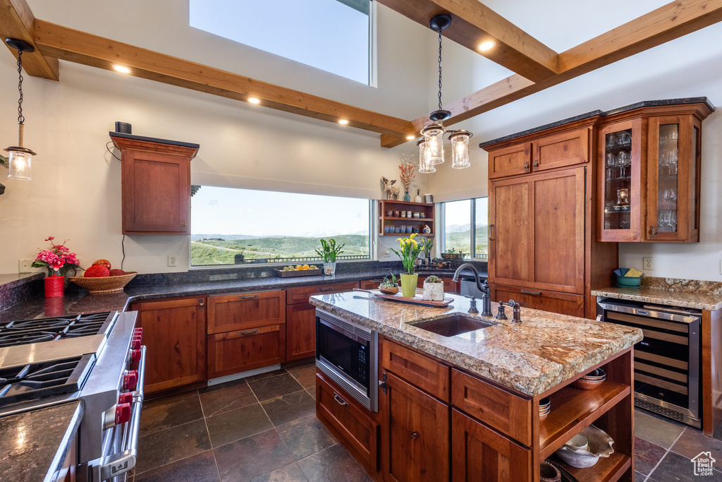 Kitchen featuring open shelves, beverage cooler, appliances with stainless steel finishes, a sink, and a kitchen island with sink