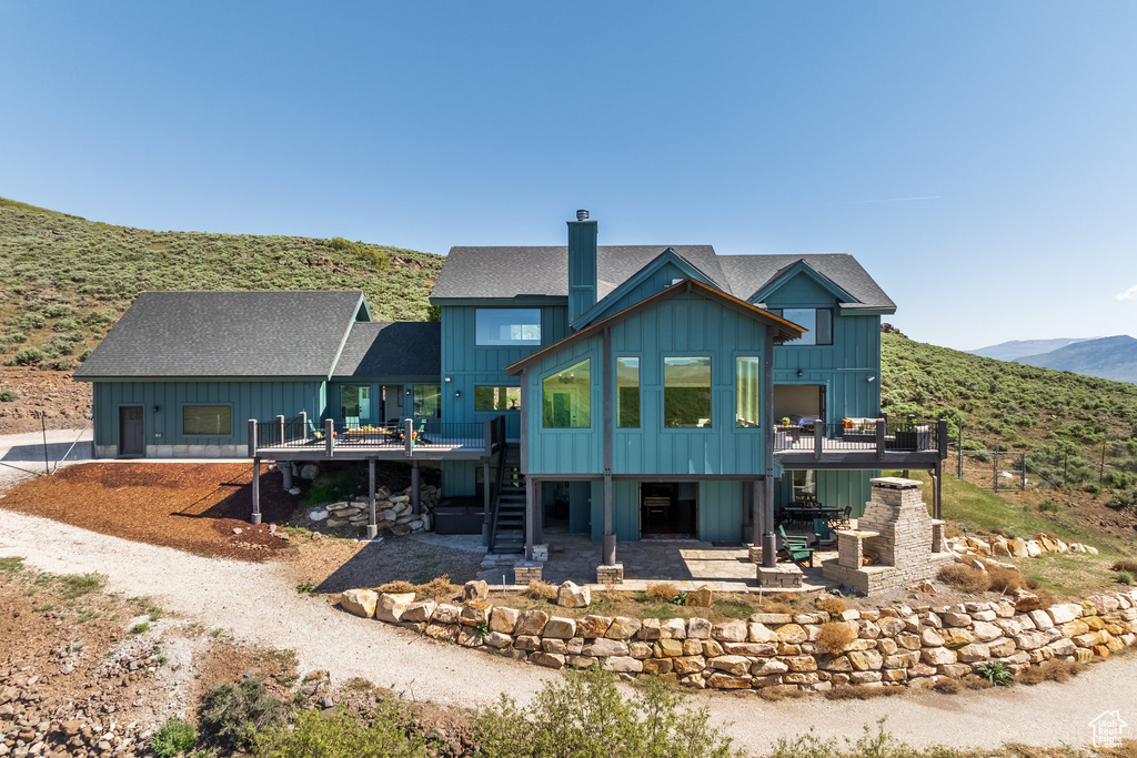 Back of house featuring stairs, board and batten siding, a deck with mountain view, a chimney, and a patio area