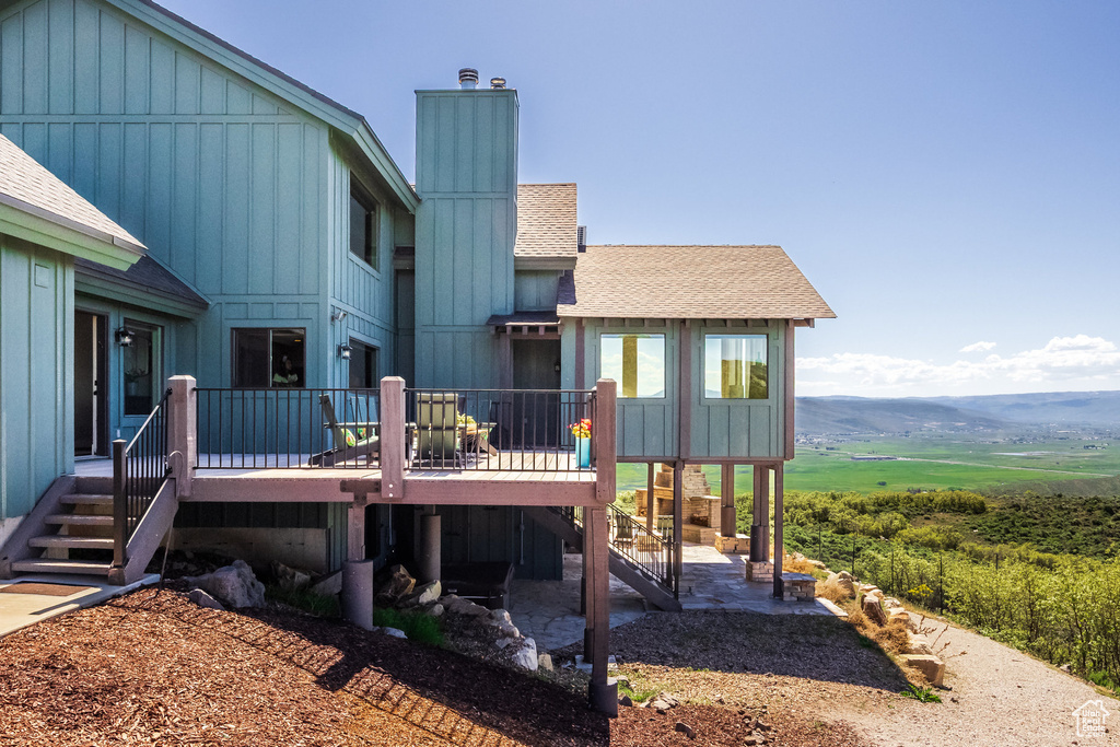 Back of property with a deck with mountain view, a shingled roof, and stairway