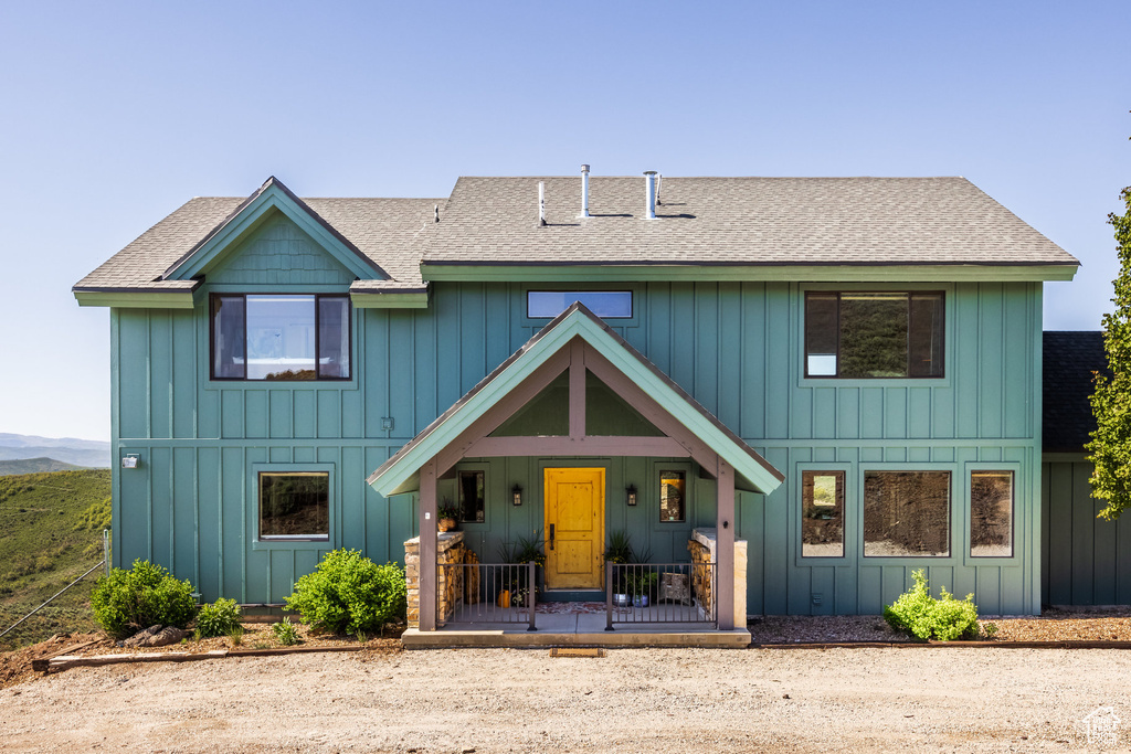 View of front facade with covered porch, roof with shingles, and board and batten siding