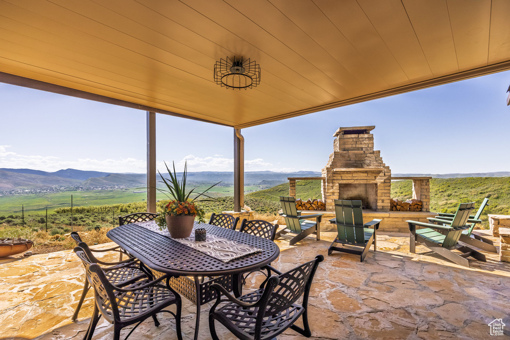 View of patio featuring an outdoor stone fireplace, a mountain view, and outdoor dining area