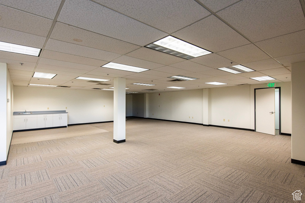 Unfurnished room with light colored carpet, a drop ceiling, a sink, and baseboards