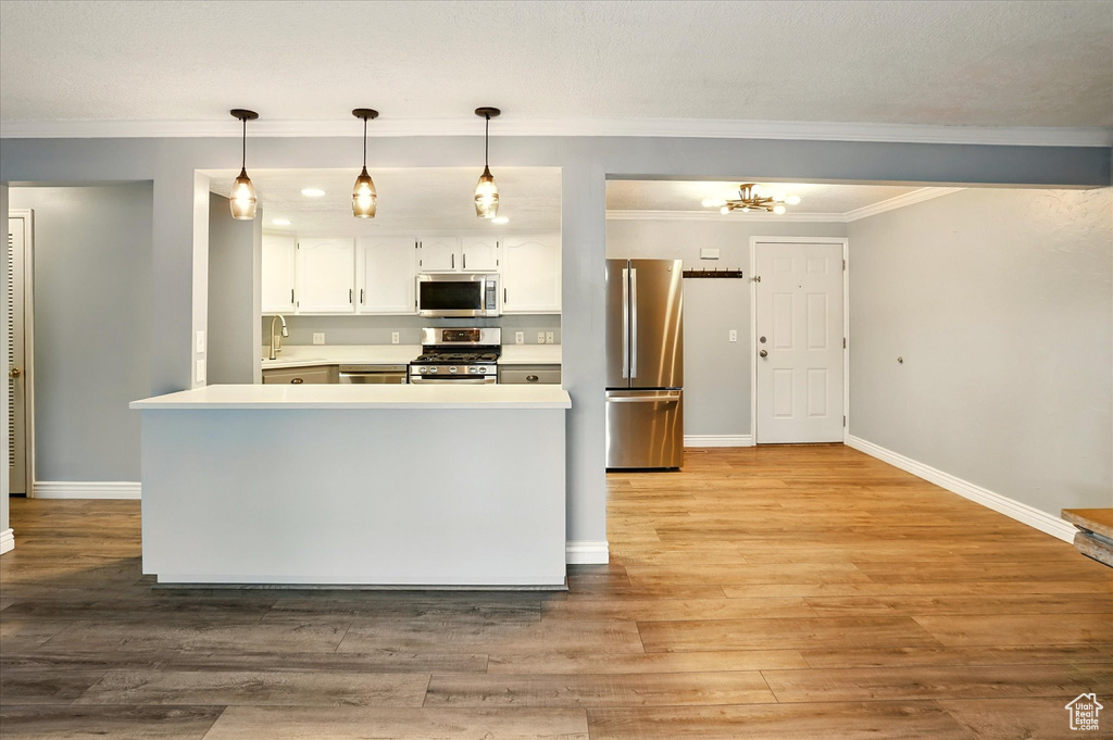 Kitchen featuring stainless steel appliances, white cabinets, light countertops, baseboards, and ornamental molding