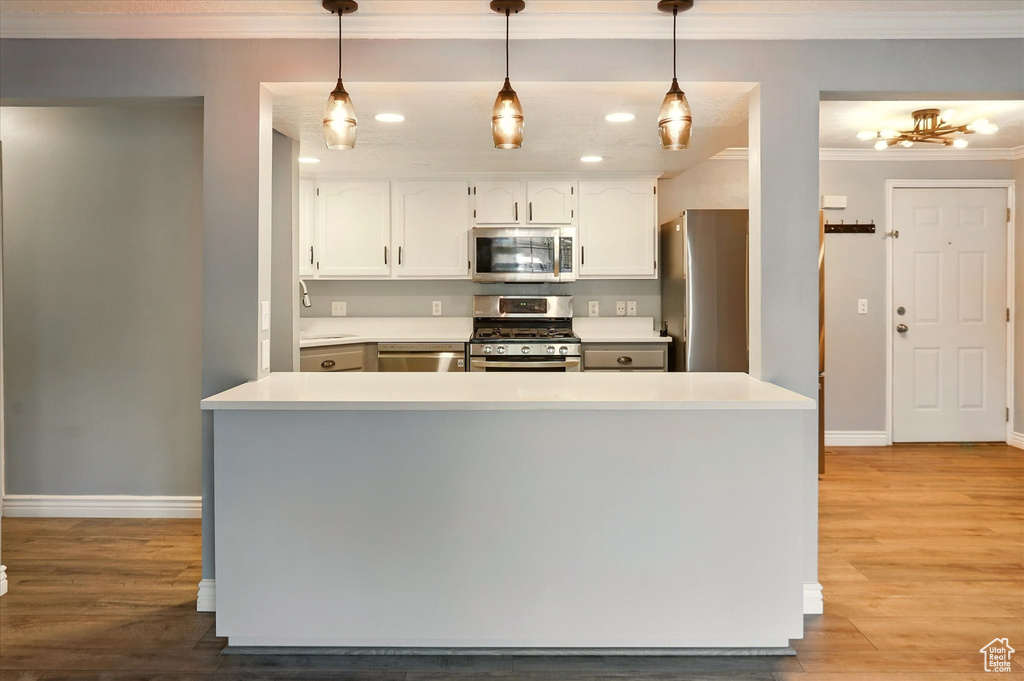 Kitchen with stainless steel appliances, crown molding, baseboards, white cabinetry, and light wood-style floors