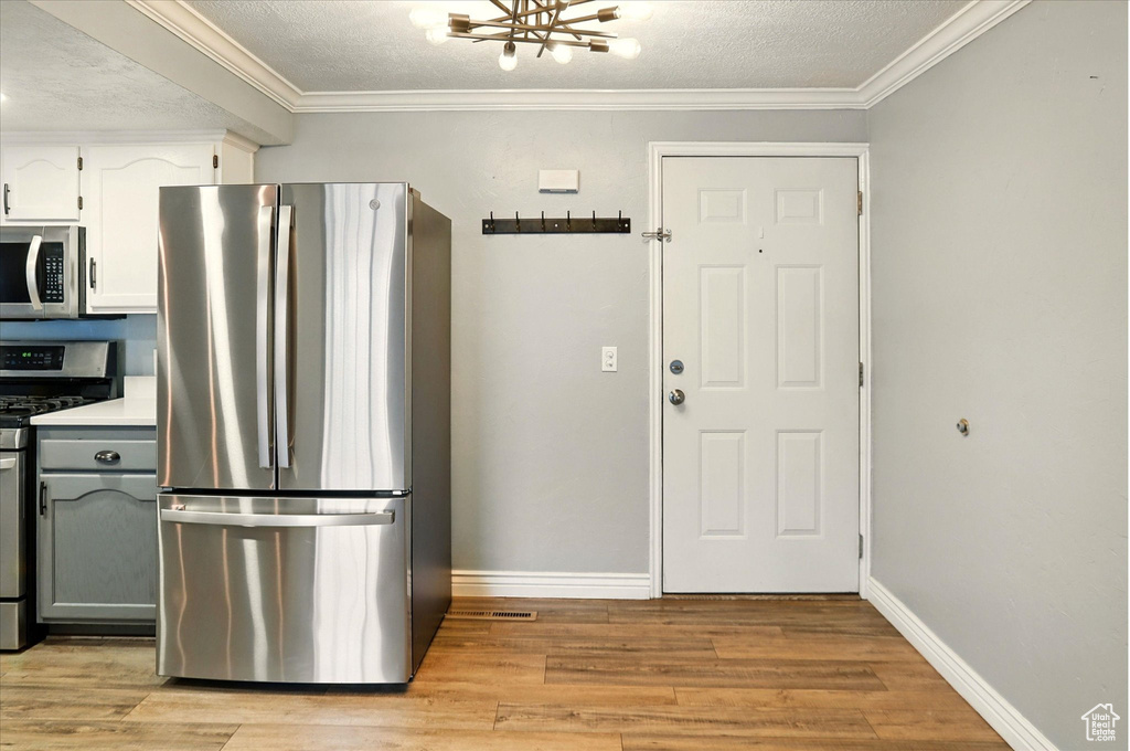 Kitchen with appliances with stainless steel finishes, light wood-type flooring, baseboards, a chandelier, and crown molding
