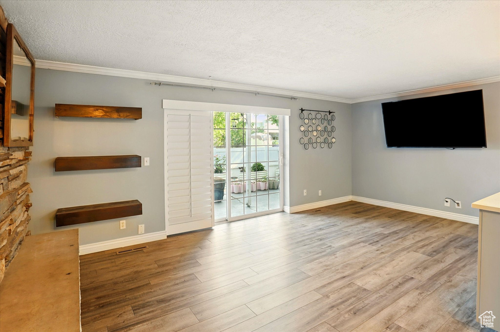 Unfurnished living room with crown molding, wood finished floors, baseboards, and a textured ceiling