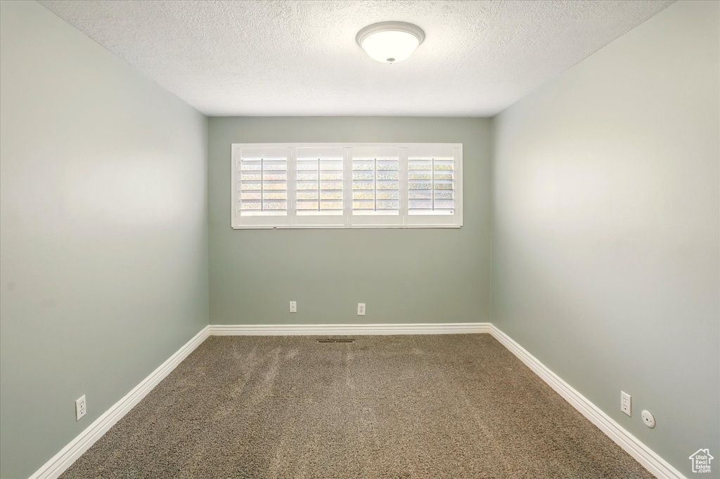 Carpeted spare room with a textured ceiling and baseboards