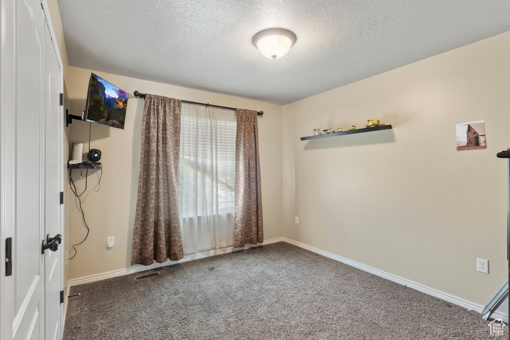 Carpeted spare room featuring a textured ceiling and baseboards