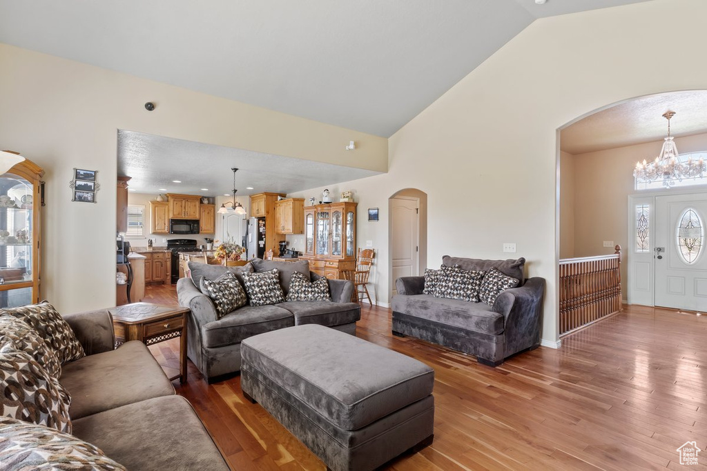 Living area with arched walkways, a chandelier, light wood-style flooring, and high vaulted ceiling