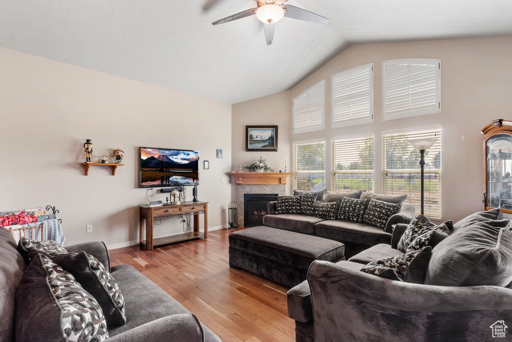 Living area with ceiling fan, high vaulted ceiling, a glass covered fireplace, light wood-type flooring, and baseboards
