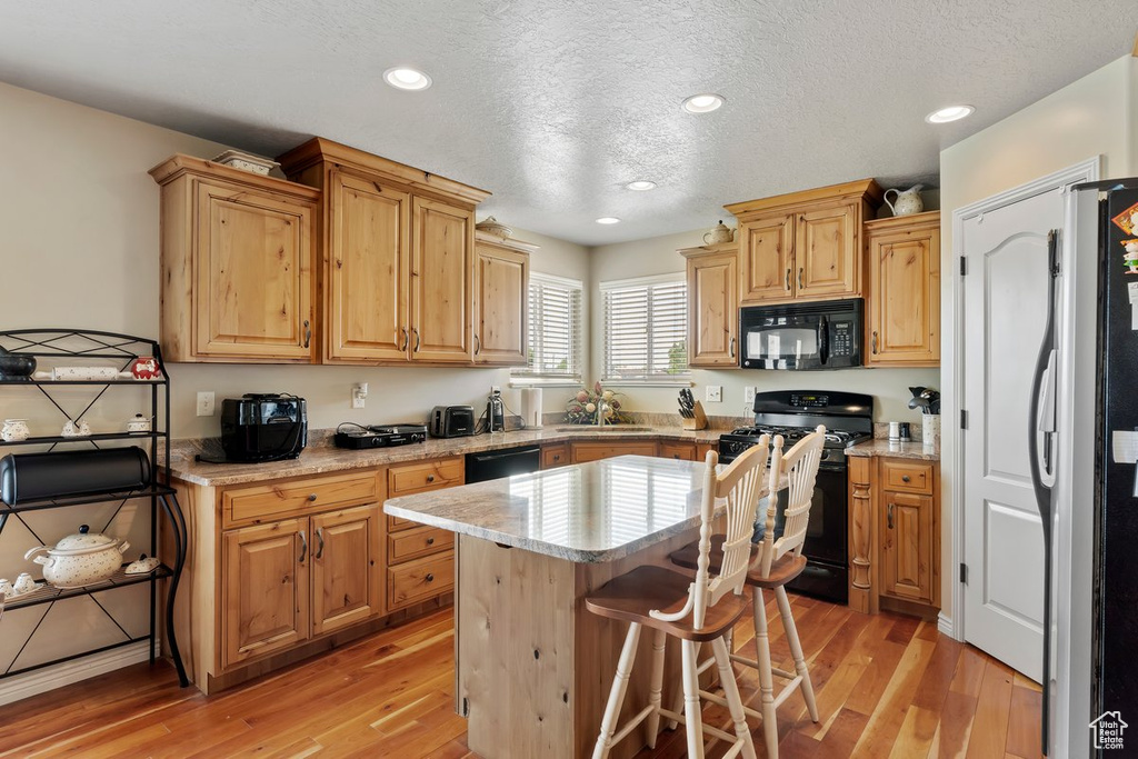 Kitchen with black appliances, a sink, light wood-type flooring, a kitchen island, and a textured ceiling