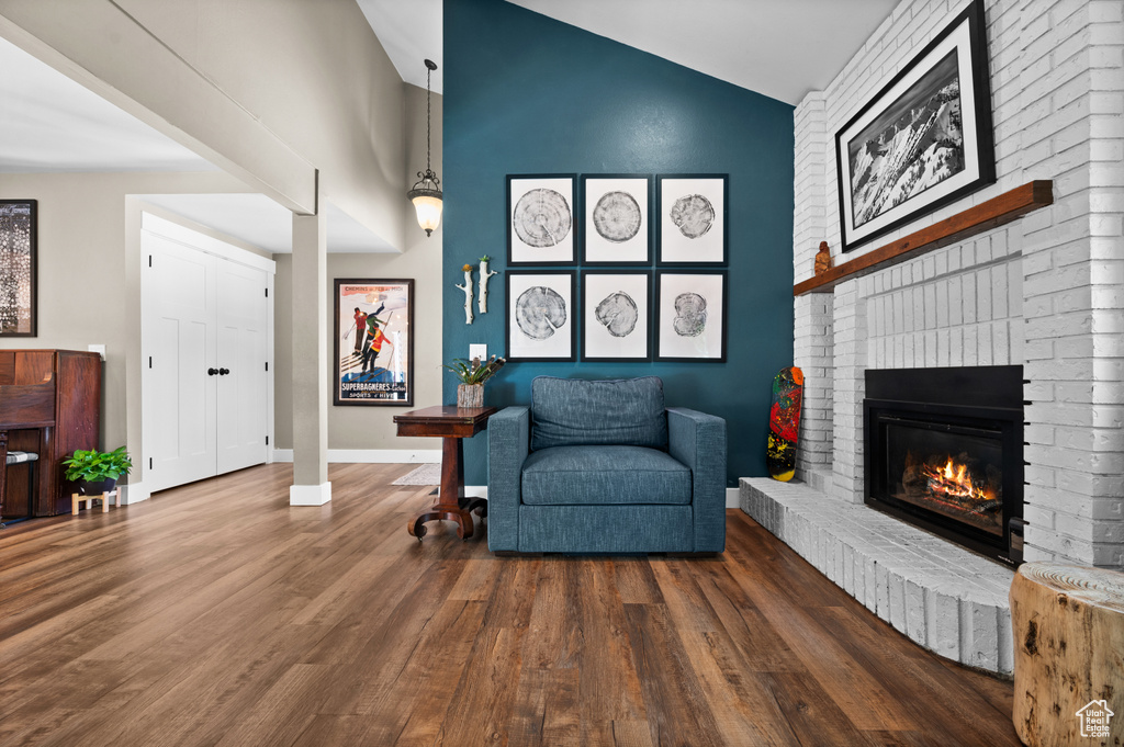 Living area featuring wood finished floors, a brick fireplace, baseboards, and high vaulted ceiling
