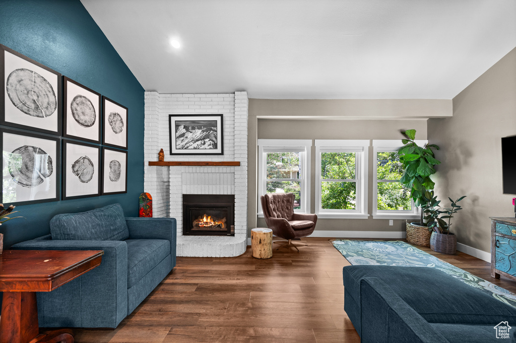 Living room with vaulted ceiling, a fireplace, wood finished floors, and baseboards