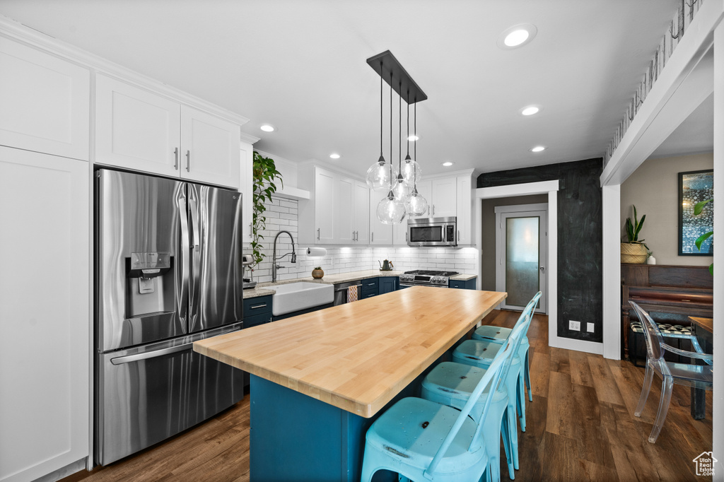 Kitchen with stainless steel appliances, wood counters, a sink, white cabinets, and recessed lighting