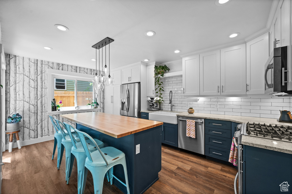 Kitchen featuring appliances with stainless steel finishes, a sink, wooden counters, a breakfast bar, and white cabinets