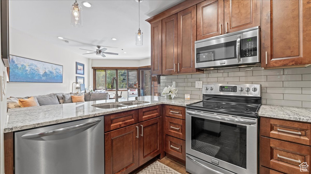 Kitchen featuring appliances with stainless steel finishes, a sink, a peninsula, decorative backsplash, and recessed lighting