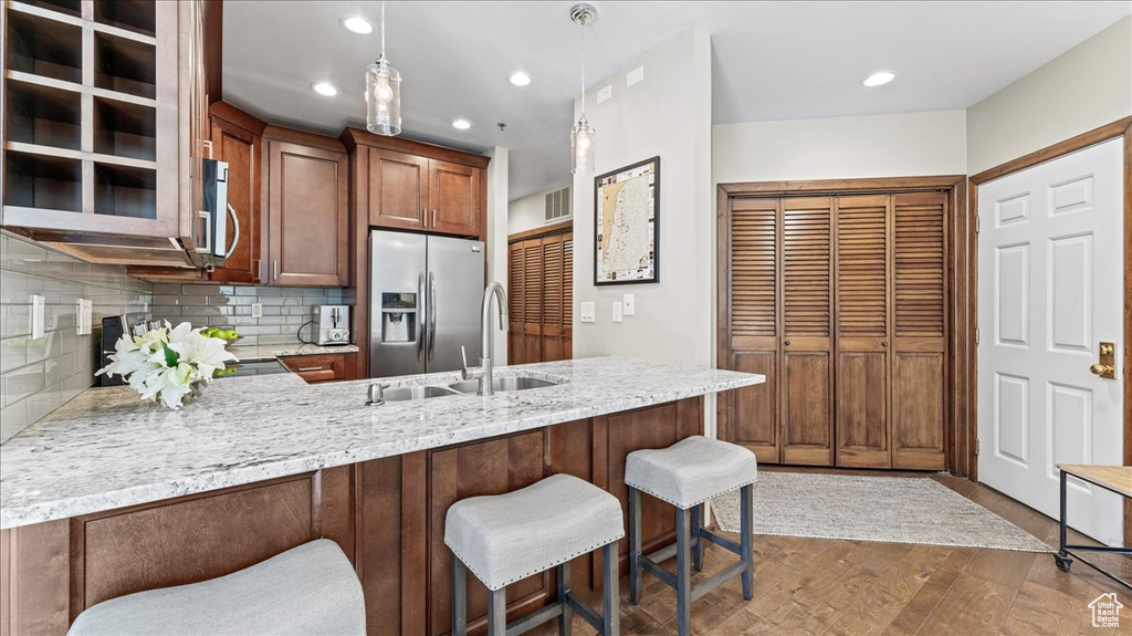 Kitchen with stainless steel appliances, a peninsula, a sink, decorative backsplash, and dark wood-style flooring