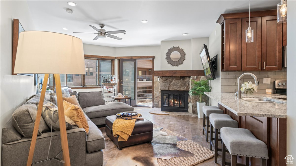 Living area featuring a ceiling fan, recessed lighting, light wood finished floors, and a stone fireplace