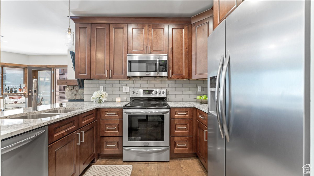Kitchen featuring stainless steel appliances, a sink, light wood-style flooring, and tasteful backsplash