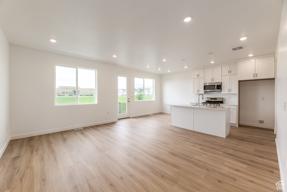 Kitchen with appliances with stainless steel finishes, open floor plan, light wood-type flooring, recessed lighting, and white cabinets