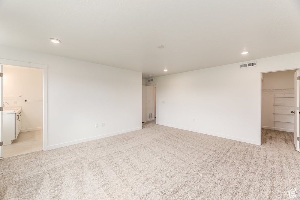 Unfurnished bedroom with a walk in closet, recessed lighting, light colored carpet, and a closet