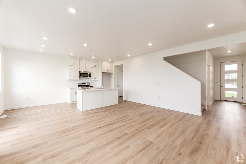 Unfurnished living room with baseboards, light wood-style flooring, recessed lighting, and a sink